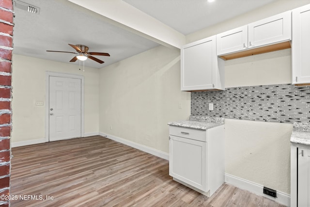 kitchen with light wood-type flooring, visible vents, a ceiling fan, decorative backsplash, and light stone countertops