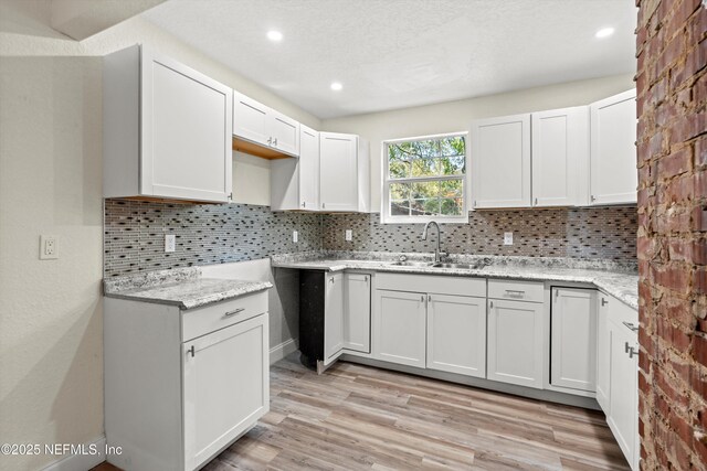 kitchen with light stone countertops, decorative backsplash, recessed lighting, light wood-style flooring, and a sink