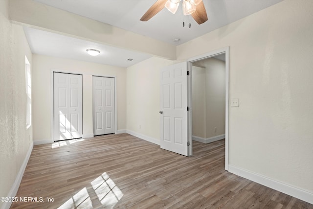 unfurnished bedroom with baseboards, light wood-type flooring, and multiple closets
