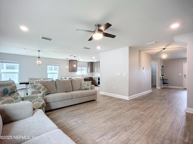 living area featuring a textured ceiling, wood finished floors, visible vents, and baseboards