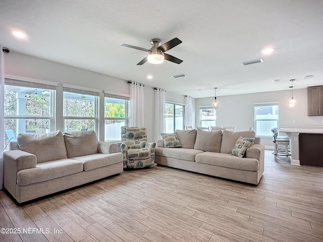 living area with light wood finished floors, visible vents, ceiling fan, a textured ceiling, and recessed lighting