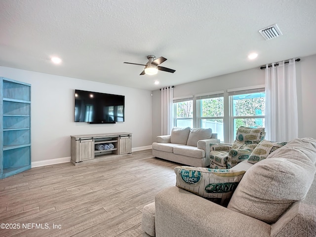 living room with visible vents, light wood-style flooring, and a textured ceiling