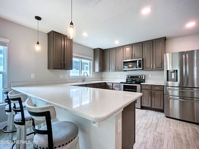 kitchen with light wood-style flooring, a peninsula, stainless steel appliances, dark brown cabinets, and a sink