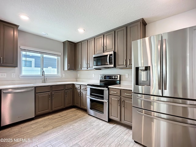 kitchen featuring light wood finished floors, appliances with stainless steel finishes, light countertops, a textured ceiling, and a sink