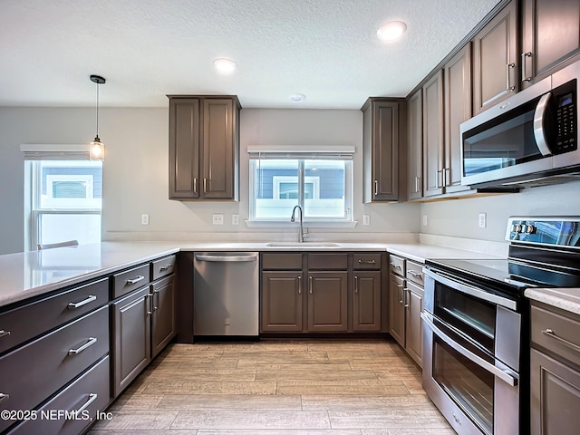 kitchen with light wood finished floors, stainless steel appliances, a textured ceiling, light countertops, and a sink