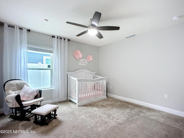 carpeted bedroom featuring a crib, visible vents, baseboards, ceiling fan, and a textured ceiling