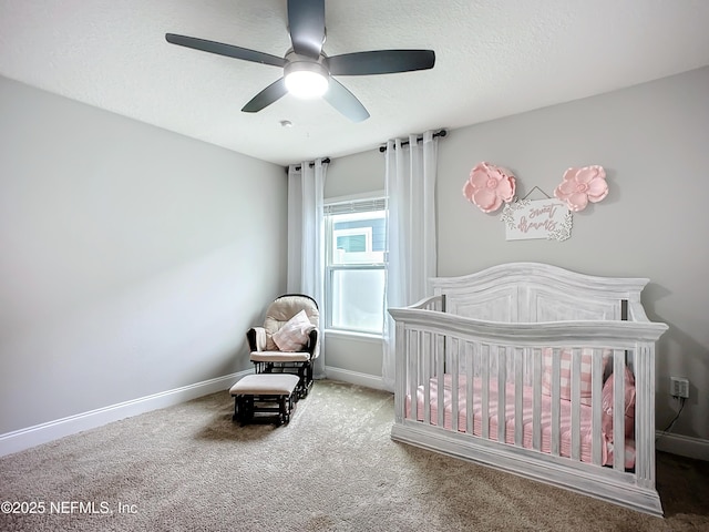 carpeted bedroom with a crib, ceiling fan, baseboards, and a textured ceiling