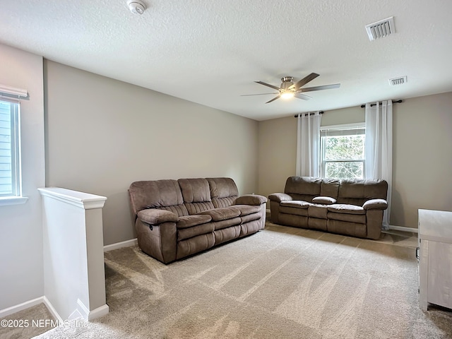 carpeted living room featuring baseboards, a textured ceiling, visible vents, and a ceiling fan