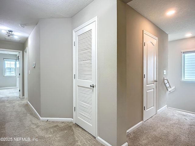 hall with a textured ceiling, baseboards, and light colored carpet