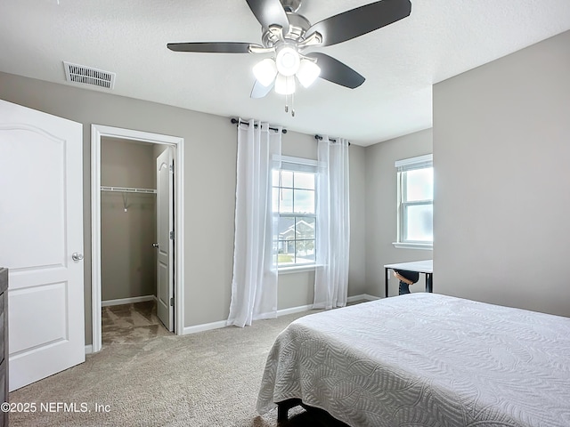 bedroom featuring baseboards, visible vents, light colored carpet, ceiling fan, and a walk in closet