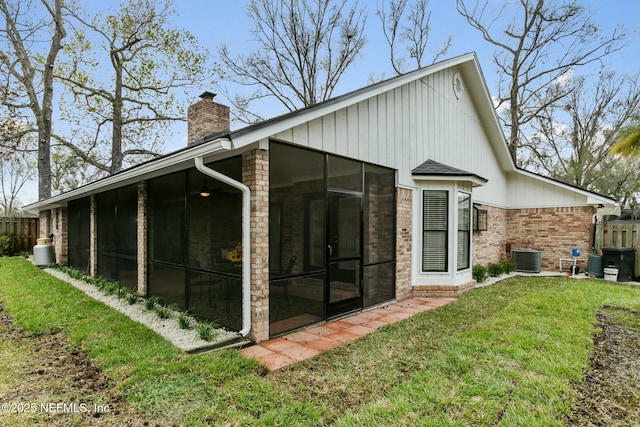 back of property with a sunroom, a chimney, fence, a yard, and brick siding