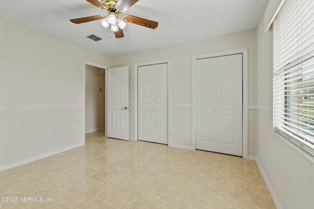 unfurnished bedroom with light tile patterned floors, a ceiling fan, baseboards, visible vents, and multiple closets