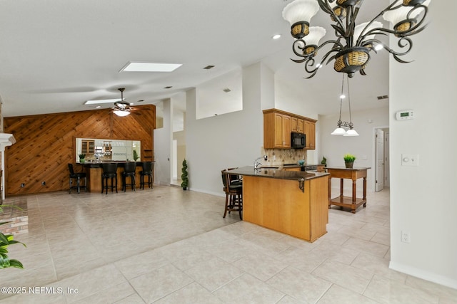 kitchen with dark countertops, a peninsula, wood walls, a kitchen bar, and black microwave