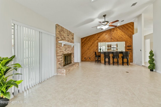 tiled living room featuring high vaulted ceiling, wood walls, a fireplace, bar area, and visible vents