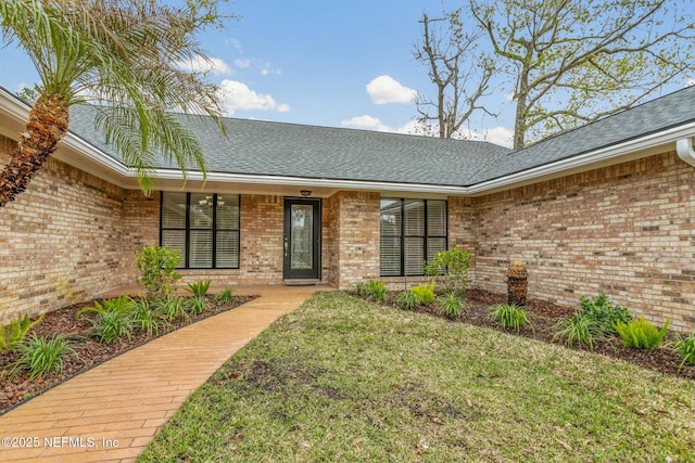 property entrance with brick siding, roof with shingles, and a lawn