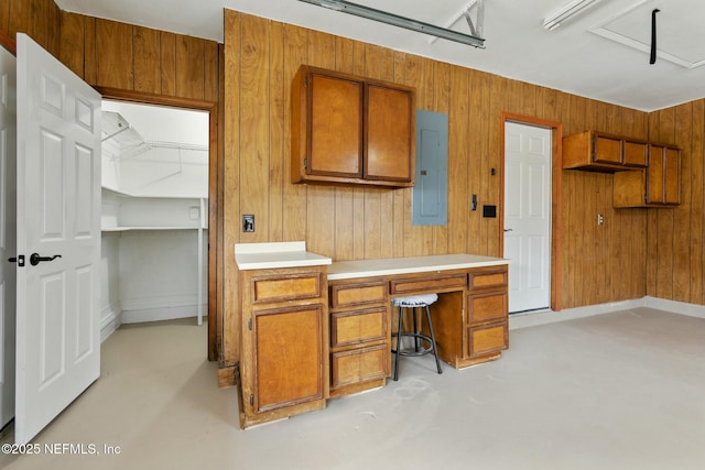 kitchen with electric panel, finished concrete floors, brown cabinetry, and light countertops