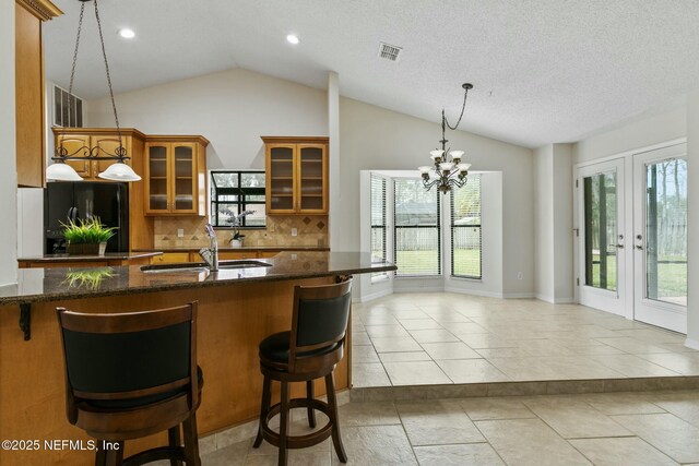 kitchen with visible vents, brown cabinets, freestanding refrigerator, vaulted ceiling, and a sink