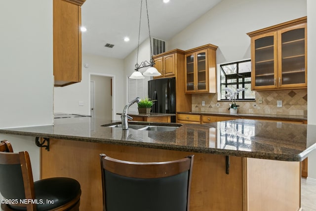 kitchen featuring brown cabinetry, lofted ceiling, freestanding refrigerator, a sink, and backsplash