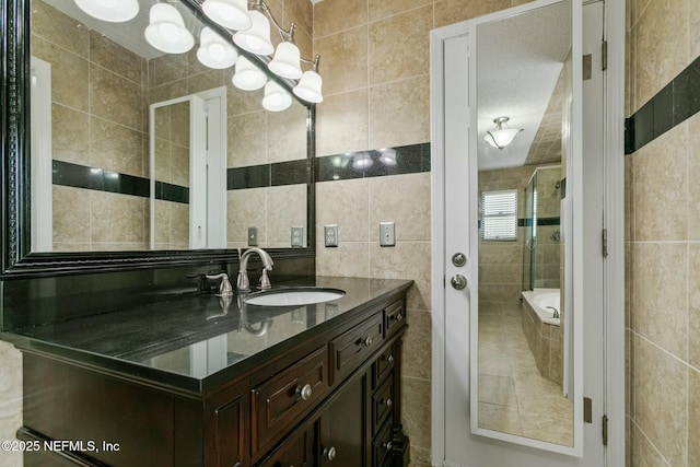 full bathroom featuring a relaxing tiled tub, an inviting chandelier, a tile shower, vanity, and tile walls