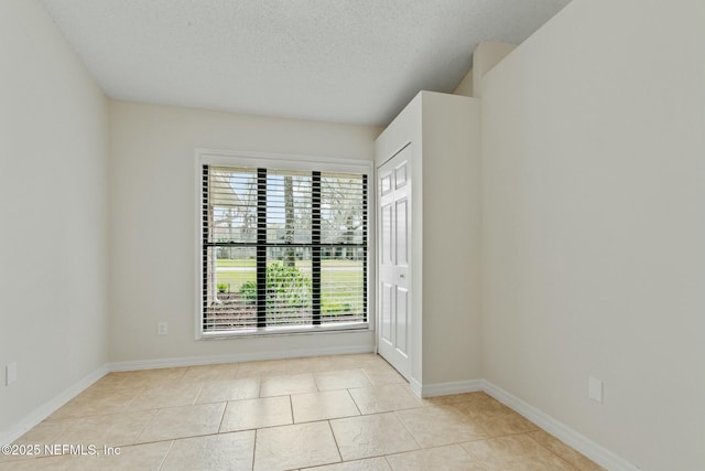 tiled empty room featuring a textured ceiling and baseboards