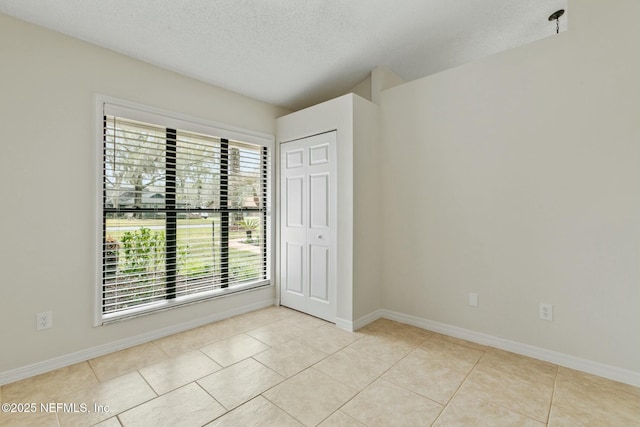 unfurnished room featuring light tile patterned floors, baseboards, and a textured ceiling