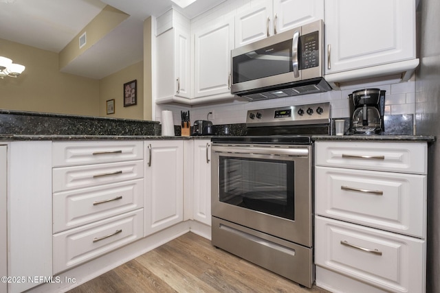 4020 Lavista Cir Unit 207, Jacksonville, FL 32217 - kitchen with dark stone counters, light wood-style flooring, appliances with stainless steel finishes, white cabinetry, and backsplash
