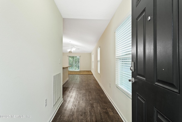 hallway featuring visible vents, baseboards, vaulted ceiling, dark wood finished floors, and an inviting chandelier