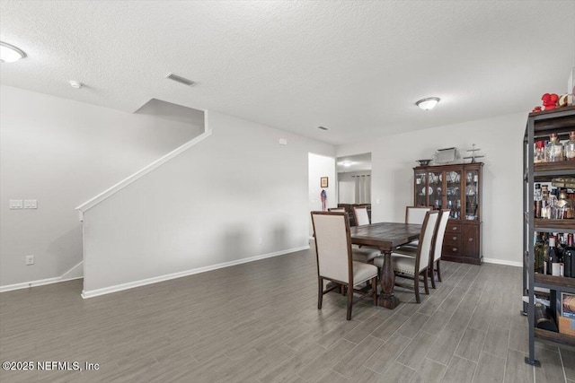 dining area with a textured ceiling, baseboards, and wood finished floors