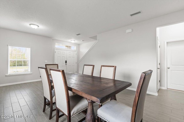 dining room with baseboards, a textured ceiling, visible vents, and wood finished floors