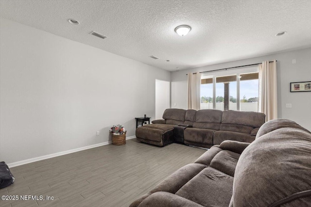 living room with visible vents, a textured ceiling, baseboards, and wood finished floors