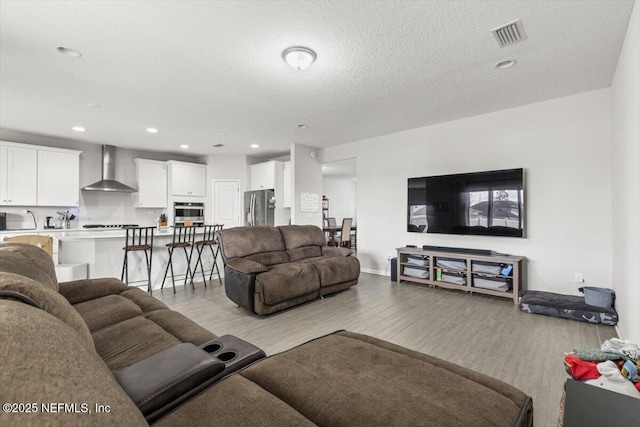 living area featuring light wood-style flooring, visible vents, a textured ceiling, and recessed lighting