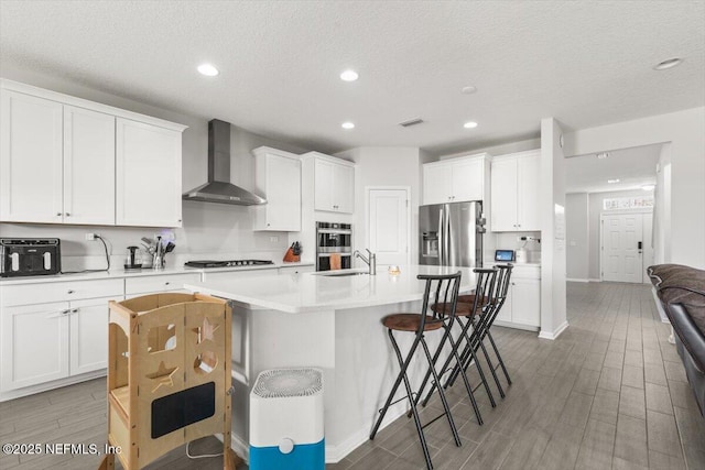 kitchen with a breakfast bar area, stainless steel appliances, light countertops, wall chimney range hood, and a sink