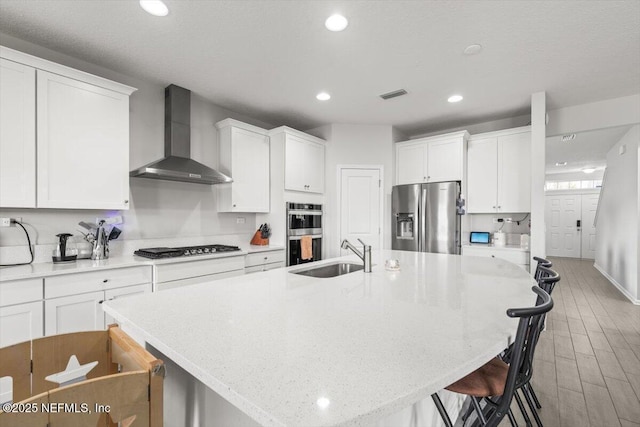 kitchen with stainless steel appliances, a sink, visible vents, a kitchen breakfast bar, and wall chimney exhaust hood