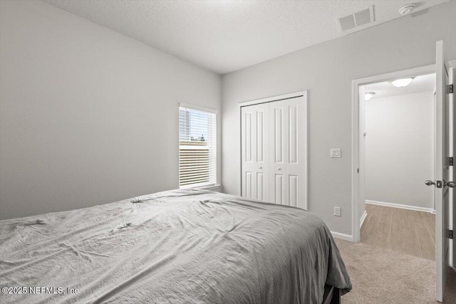 bedroom with a textured ceiling, visible vents, baseboards, a closet, and carpet