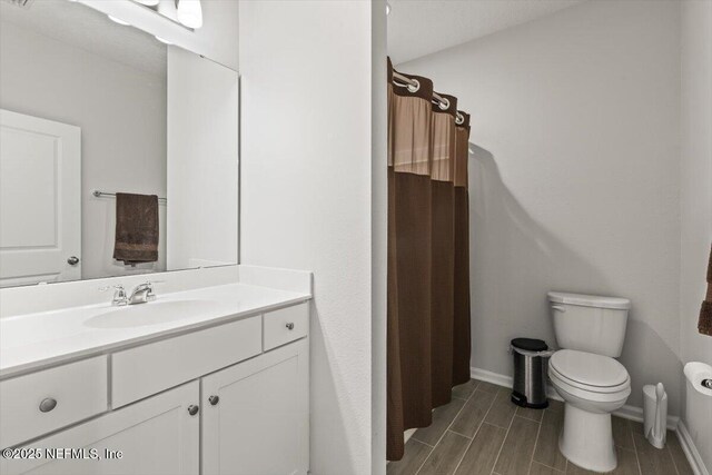 bathroom featuring baseboards, a shower with shower curtain, toilet, wood tiled floor, and vanity