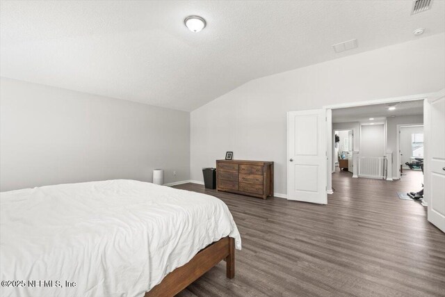 bedroom with a textured ceiling, visible vents, baseboards, vaulted ceiling, and dark wood finished floors