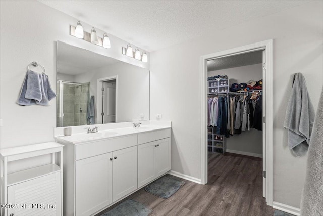 full bathroom featuring a walk in closet, a sink, a shower stall, a textured ceiling, and wood finished floors