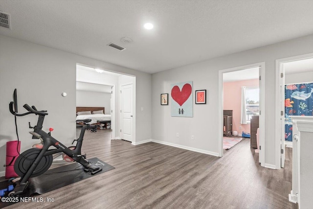 exercise area with visible vents, a textured ceiling, baseboards, and wood finished floors