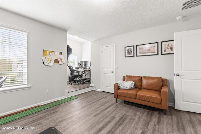 sitting room with a textured ceiling, wood finished floors, visible vents, and baseboards