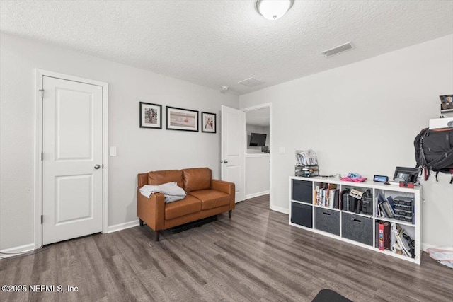 sitting room with a textured ceiling, wood finished floors, visible vents, and baseboards