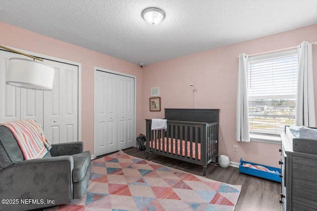 bedroom featuring multiple closets, a textured ceiling, wood finished floors, a crib, and baseboards