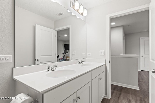 full bath with double vanity, visible vents, a sink, and wood finished floors