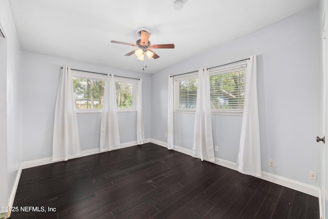 unfurnished room featuring dark wood-style floors, a ceiling fan, and baseboards