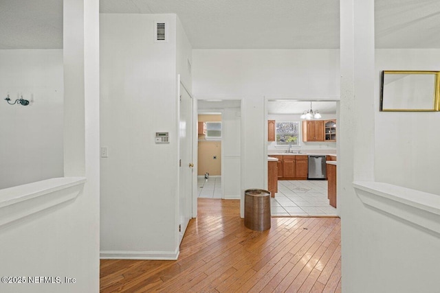 hall featuring light wood finished floors, visible vents, baseboards, a notable chandelier, and a sink