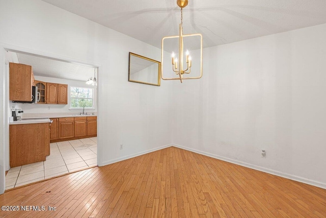 unfurnished dining area with a sink, baseboards, an inviting chandelier, and light wood finished floors