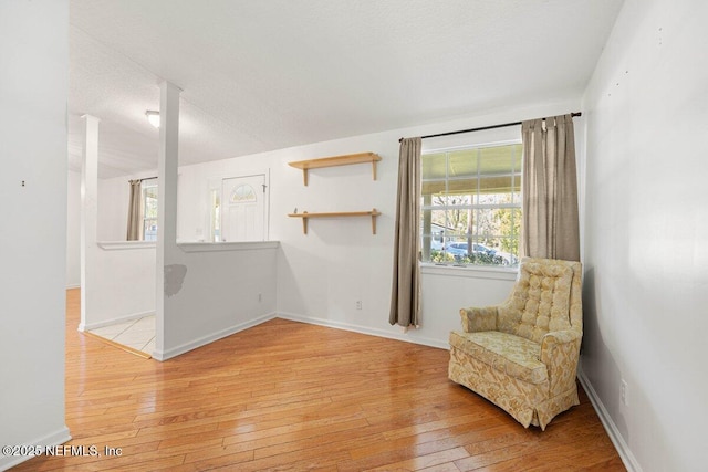 living area with baseboards, light wood-style floors, and a textured ceiling