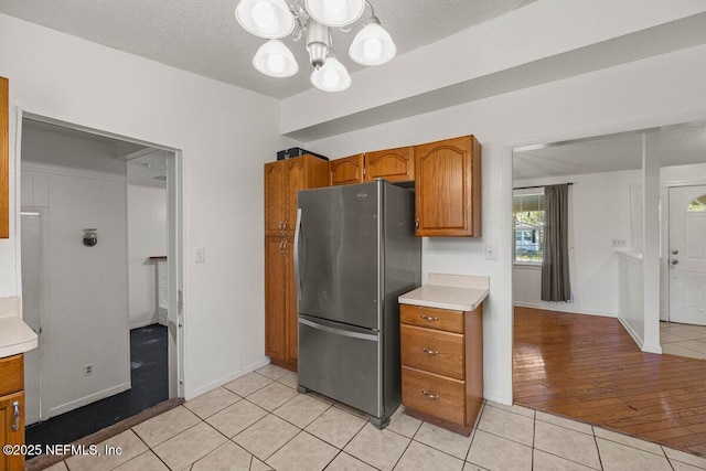 kitchen featuring brown cabinetry, light tile patterned flooring, freestanding refrigerator, light countertops, and a chandelier