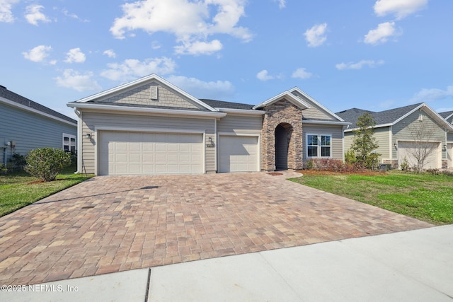 view of front facade with a garage, stone siding, decorative driveway, and a front yard