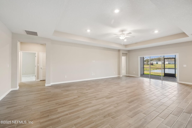 unfurnished living room with baseboards, visible vents, a ceiling fan, wood tiled floor, and a tray ceiling