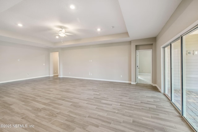 spare room featuring ceiling fan, a tray ceiling, light wood finished floors, and baseboards